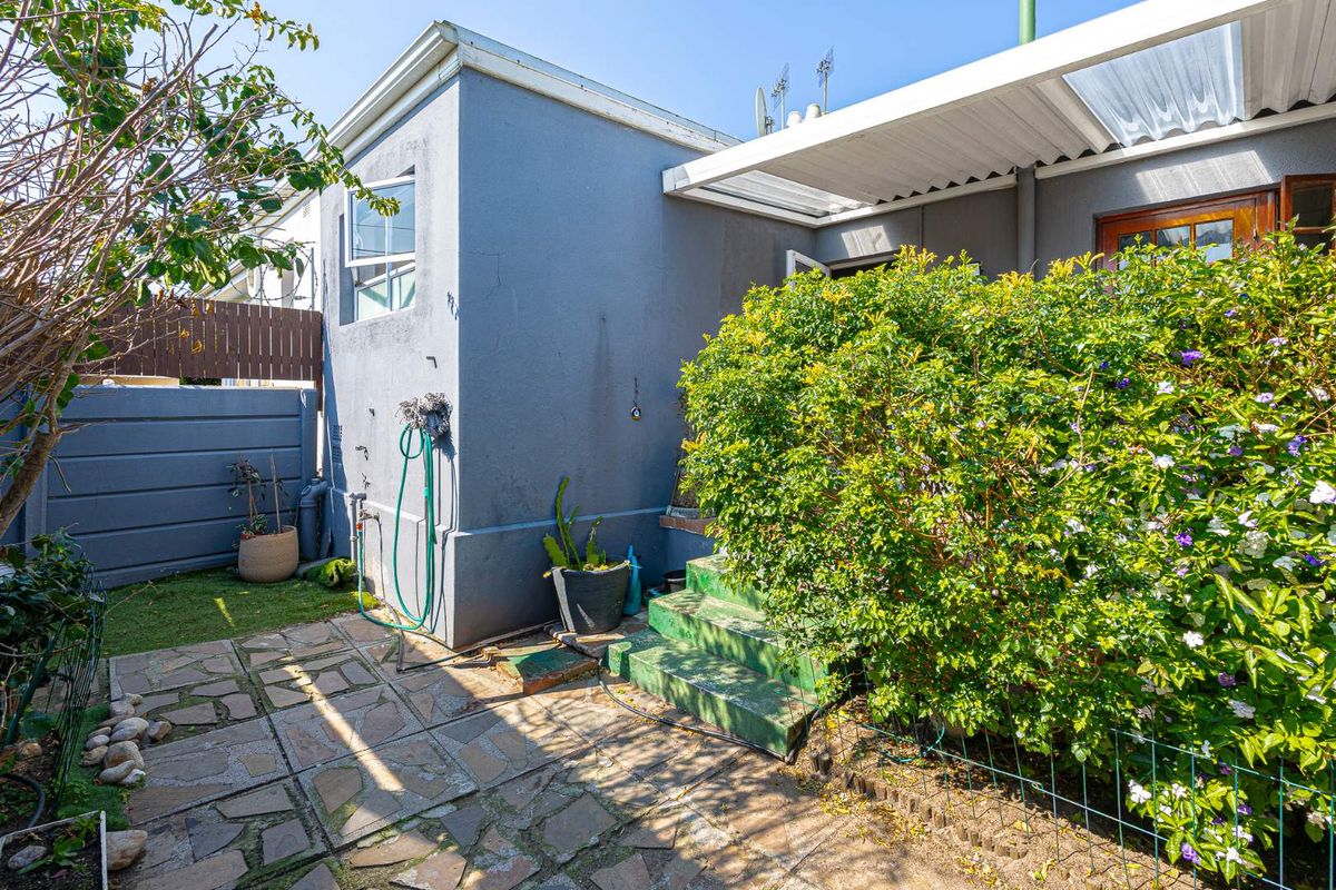 A rear exterior view featuring a paved patio area, covered veranda, and concrete steps leading to the house entrance.