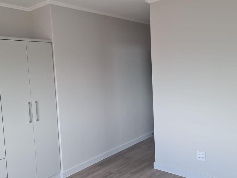 A clean, neutral bedroom featuring modern laminate flooring and a built-in wardrobe, offering a blank canvas for personalization.