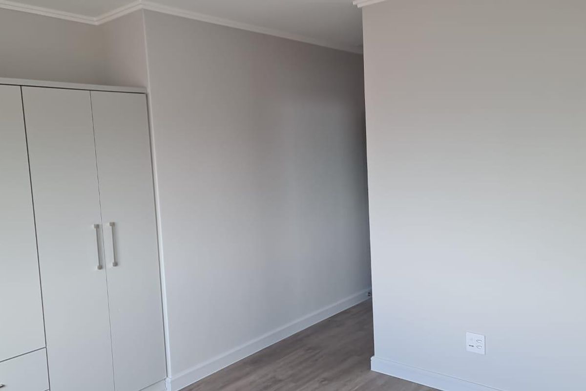 A clean, neutral bedroom featuring modern laminate flooring and a built-in wardrobe, offering a blank canvas for personalization.