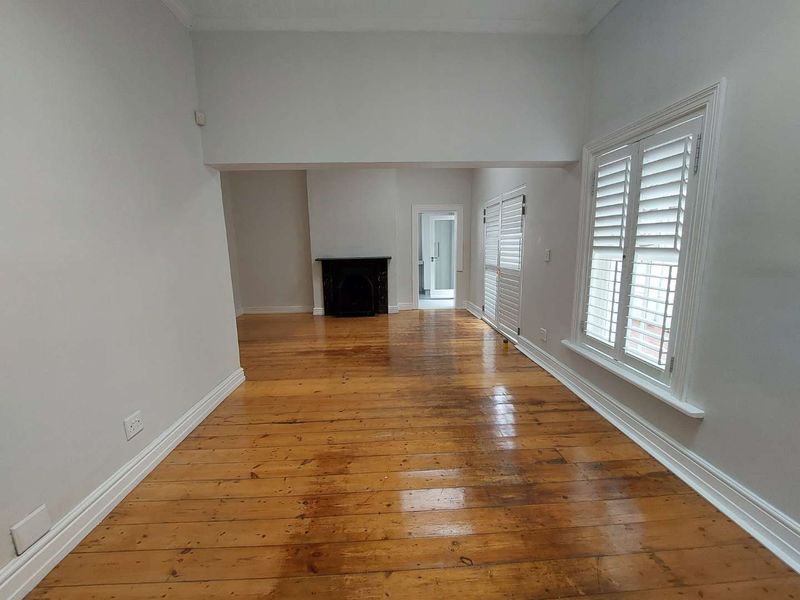 Spacious living room featuring polished hardwood flooring, a classic fireplace, and white plantation shutters, offering a bright and neutral canvas.