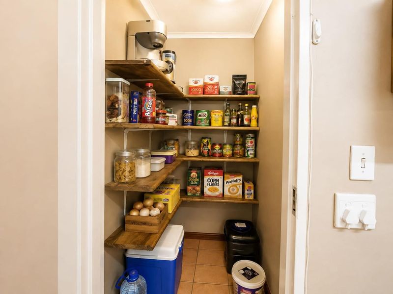 A compact walk-in pantry or scullery area featuring built-in wooden shelving and tiled flooring, providing efficient storage space.