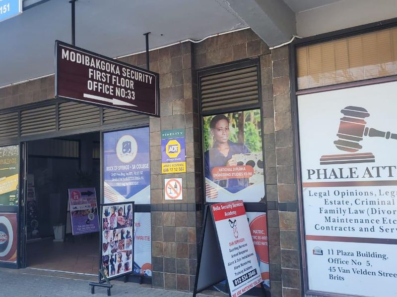 Front entrance of a commercial building featuring tiled facade, hanging signage, and multiple business advertisements displayed on the glass storefront.