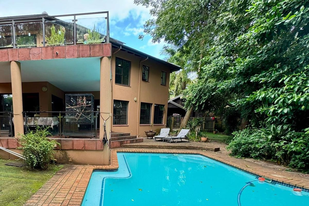 Rear view of the property featuring a swimming pool, paved patio area, and a covered balcony overlooking the garden.