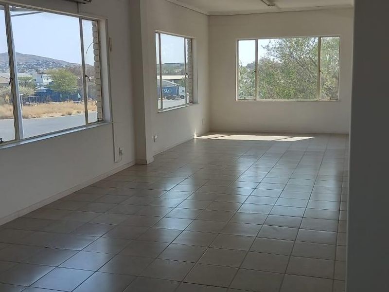 A spacious, empty office area featuring tiled flooring, large windows providing natural light, and an integrated air conditioning unit.