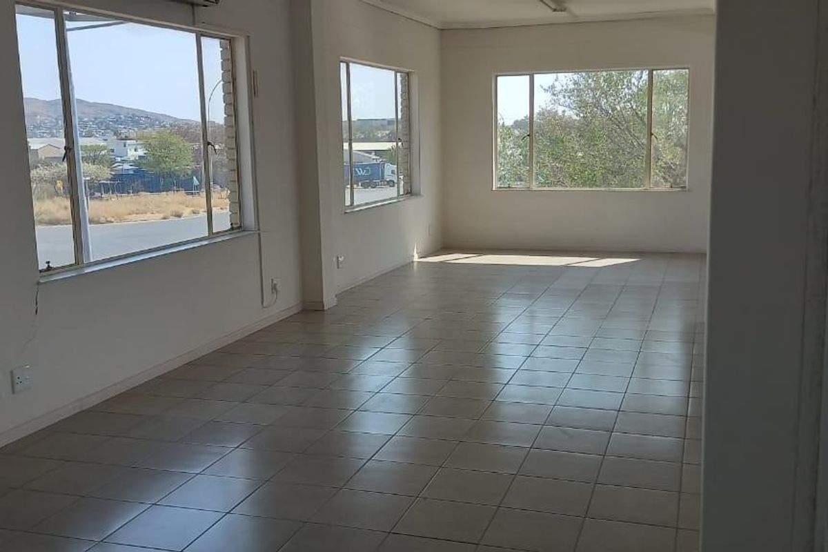 A spacious, empty office area featuring tiled flooring, large windows providing natural light, and an integrated air conditioning unit.