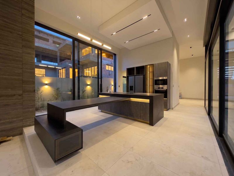 Modern, high-end kitchen featuring a large central island, integrated appliances, recessed ceiling lighting, and expansive sliding glass doors opening to an outdoor area.