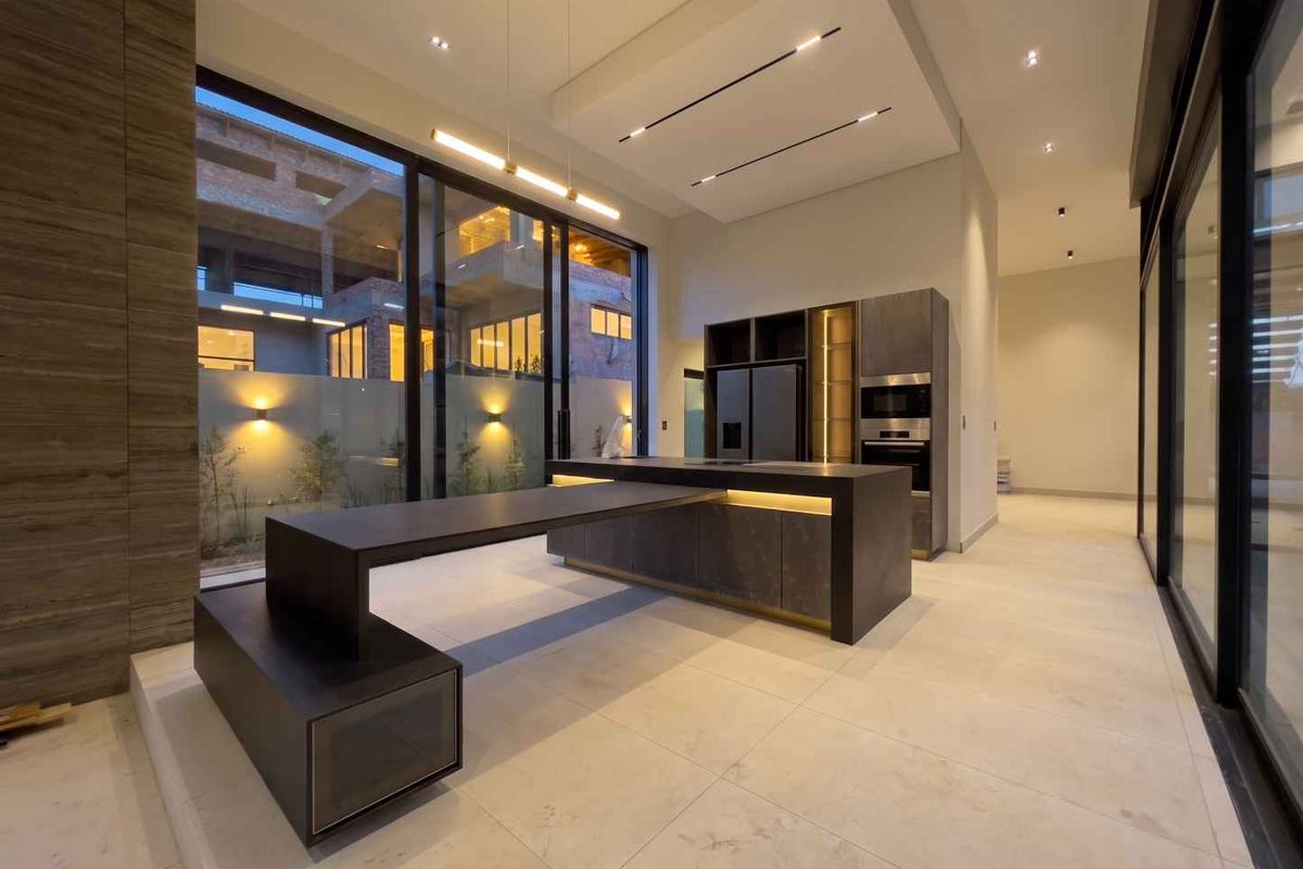 Modern, high-end kitchen featuring a large central island, integrated appliances, recessed ceiling lighting, and expansive sliding glass doors opening to an outdoor area.