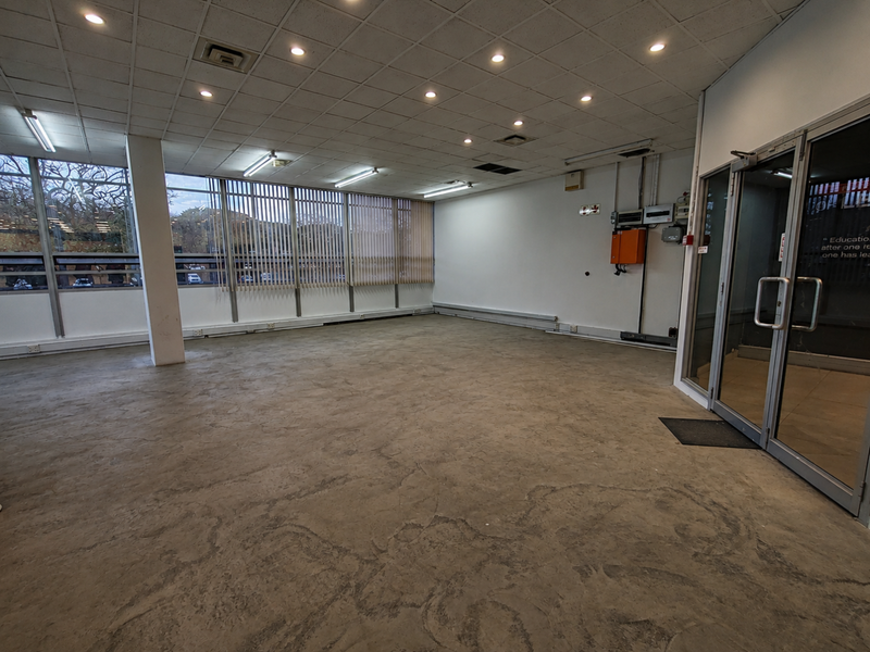 Spacious open-plan office area featuring large windows with vertical blinds, suspended ceiling with recessed lighting, and durable concrete flooring.