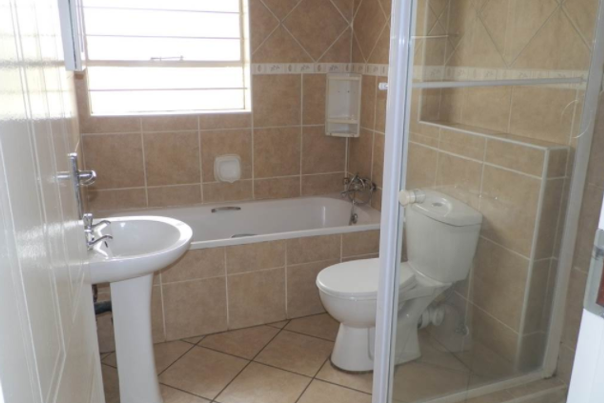 A functional bathroom featuring a pedestal basin, built-in bathtub, toilet, and a separate shower enclosure with tiled walls and flooring.