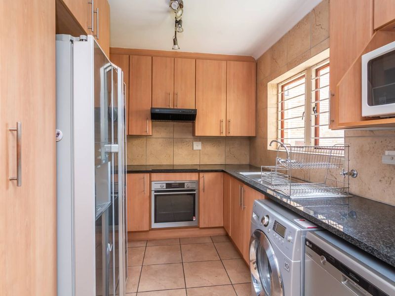 A functional kitchen featuring light wood cabinetry, granite countertops, built-in oven, extractor fan, and tiled finishes with integrated appliance space.
