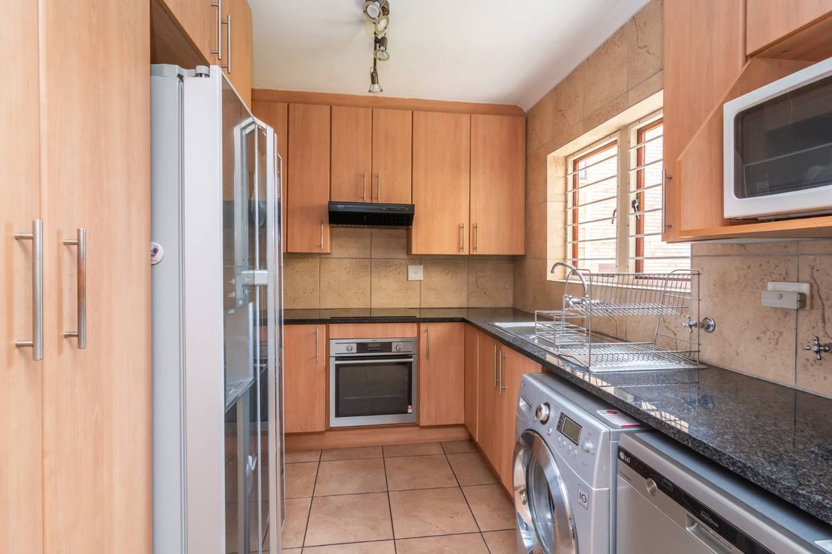 A functional kitchen featuring light wood cabinetry, granite countertops, built-in oven, extractor fan, and tiled finishes with integrated appliance space.