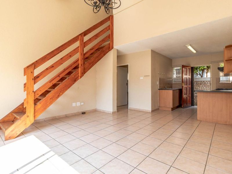 Open-plan living area featuring tiled floors, a wooden staircase, and a functional kitchen with built-in cabinetry and appliances.