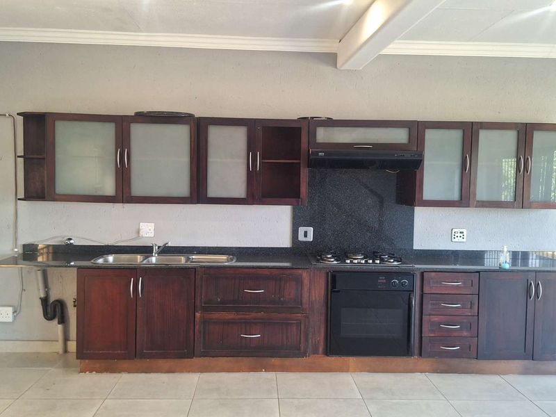 A functional kitchen featuring dark wood cabinetry, granite countertops, built-in oven, gas hob, and extractor fan, set against a neutral tiled floor.