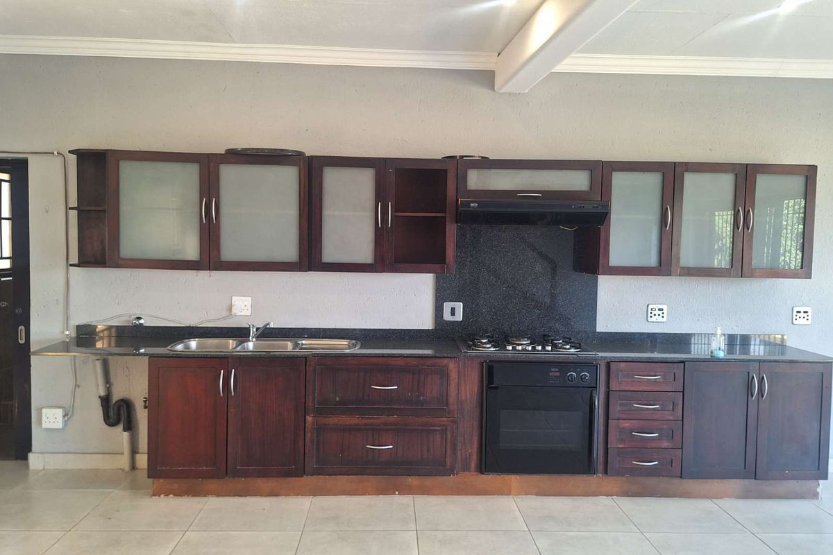 A functional kitchen featuring dark wood cabinetry, granite countertops, built-in oven, gas hob, and extractor fan, set against a neutral tiled floor.