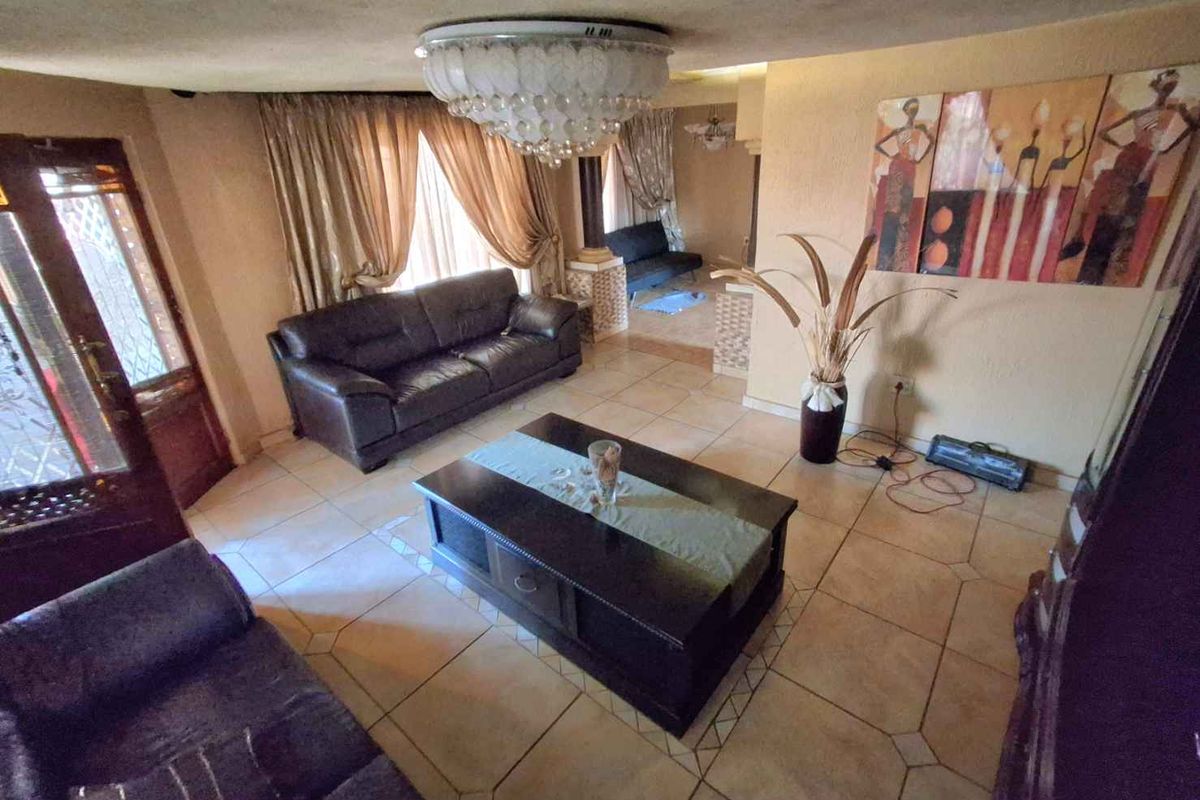Spacious living area featuring tiled flooring, decorative ceiling lighting, and an open-plan layout connecting to an adjacent room.