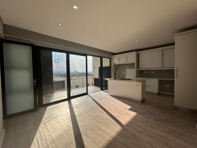 Modern open-plan kitchen and living area featuring sleek built-in cabinetry, a central island, and large sliding doors opening to a balcony with expansive views.