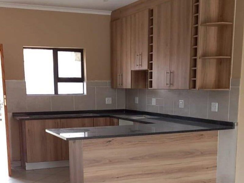 A clean, modern kitchen featuring wood-finish cabinetry, stone countertops, and neutral tiled flooring, offering a functional and well-maintained workspace.