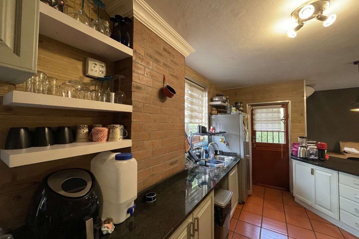 A functional kitchen featuring granite countertops, exposed brick accents, timber wall cladding, and terracotta floor tiles with direct access to the exterior.