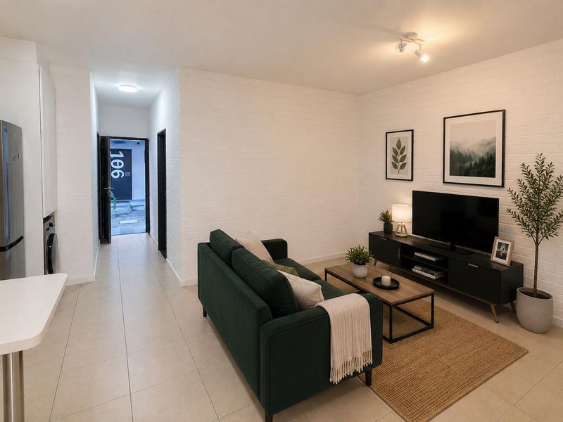 An open-plan living area featuring tiled floors, white exposed brick walls, and modern recessed lighting, creating a bright and functional apartment space.