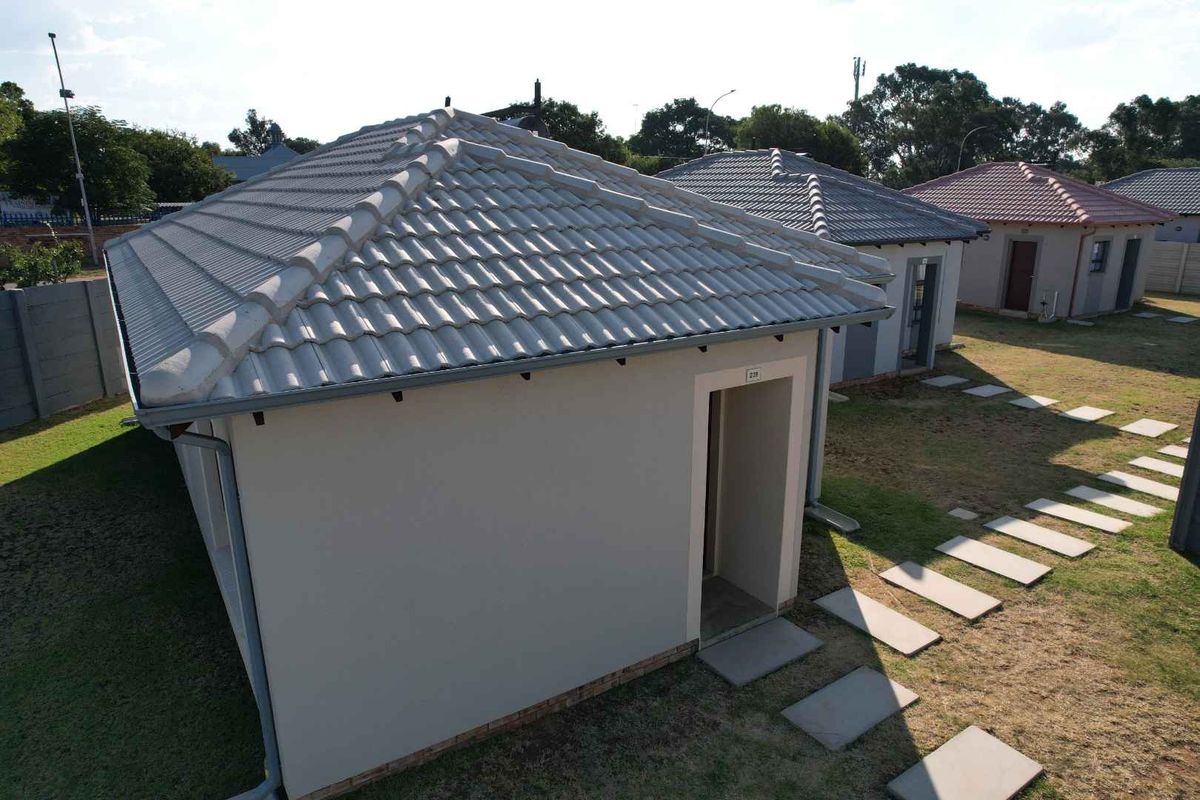 Aerial view of the rear exterior of the house featuring a tiled roof, concrete paver walkway, and surrounding garden area.