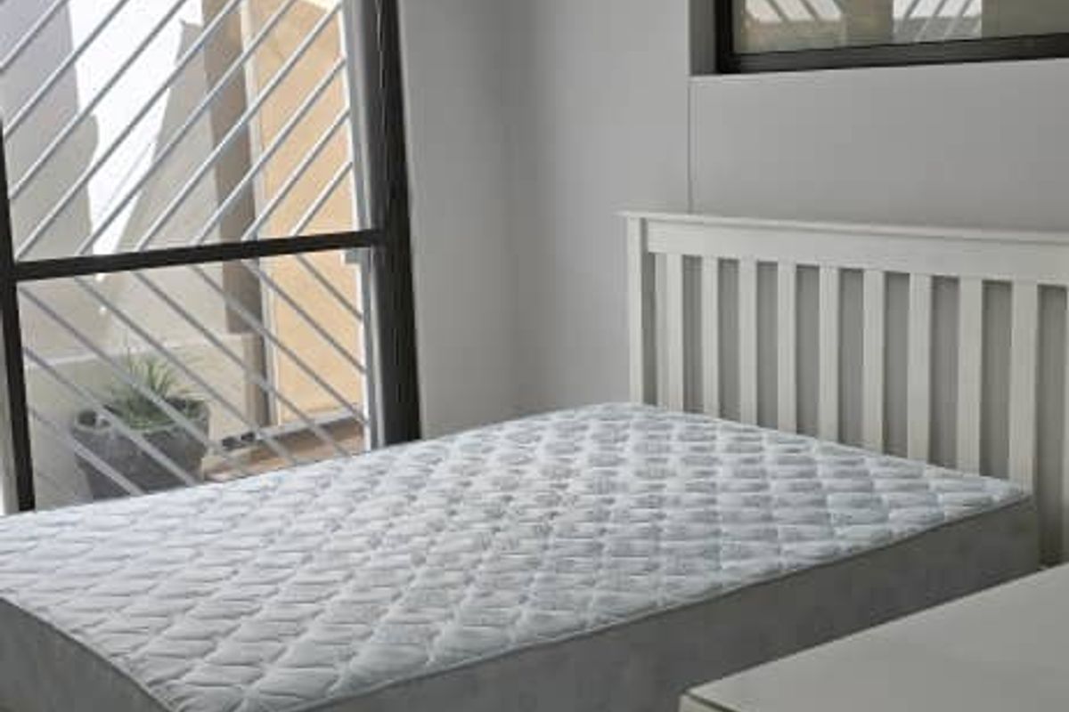 A bright bedroom featuring tiled flooring, an air conditioning unit, and a sliding door with security bars.
