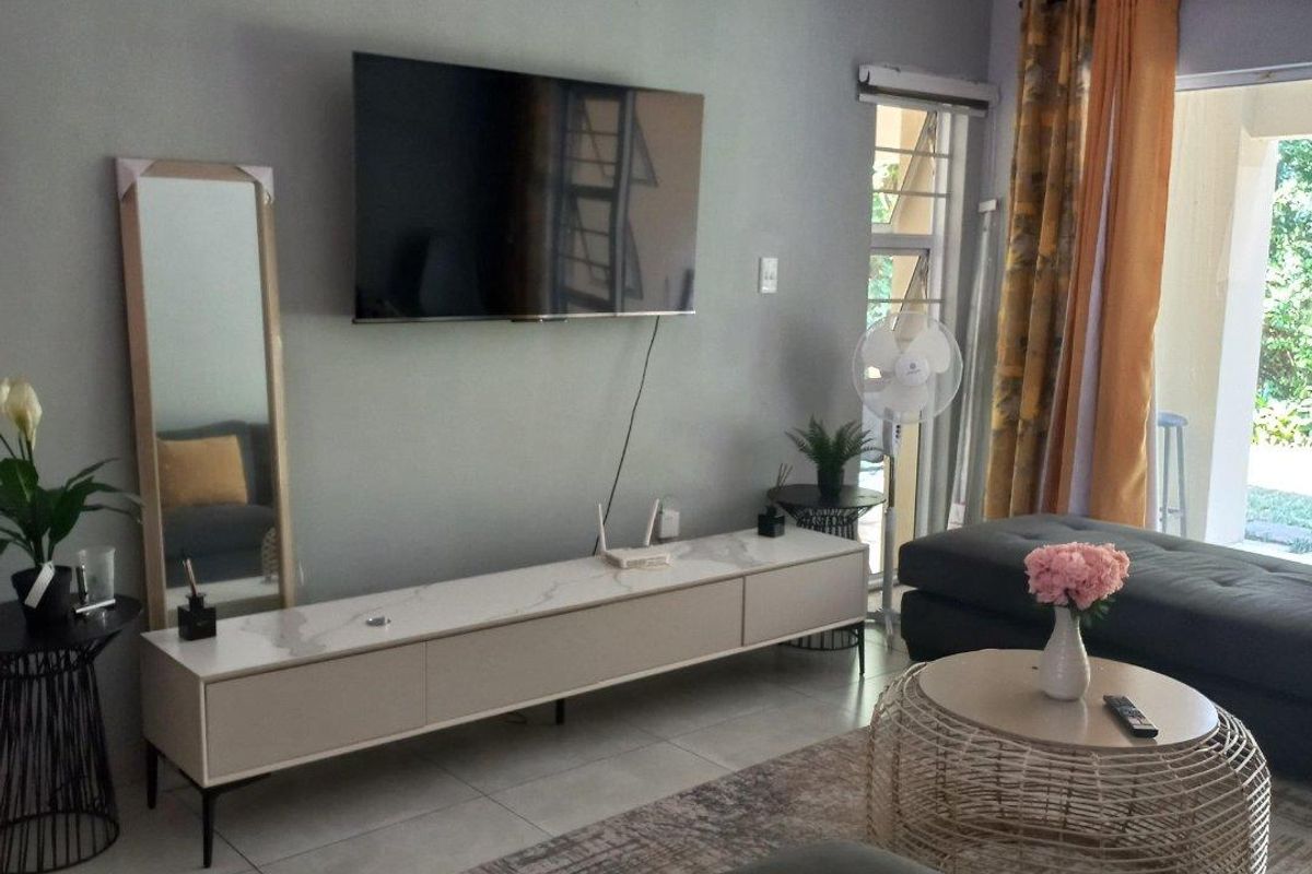 A well-maintained living room featuring neutral tiled flooring, grey walls, and a sliding door providing access to an outdoor patio area.