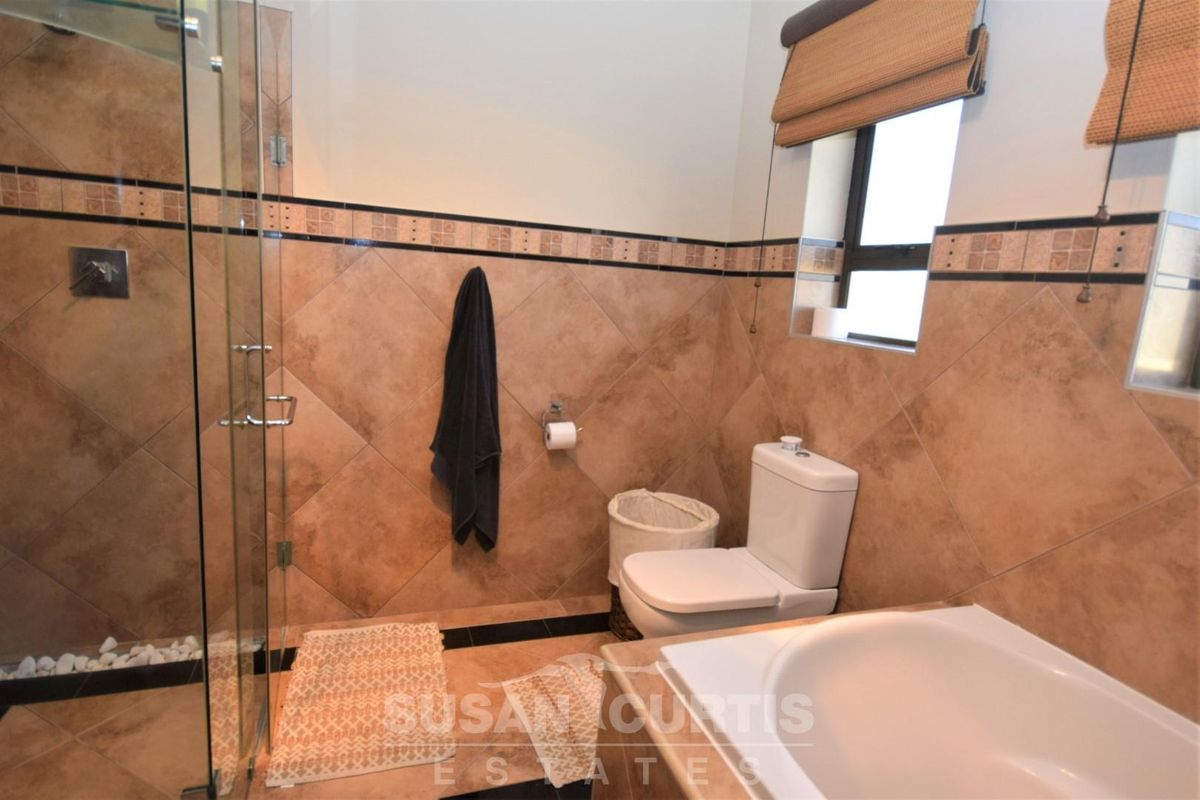 A functional bathroom featuring a glass-enclosed shower, a built-in bathtub, and tiled wall finishes with a neutral color palette.