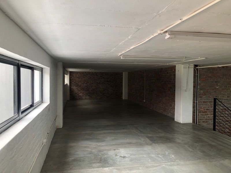A spacious, industrial-style open plan area featuring exposed brick walls, polished concrete flooring, and an exposed concrete ceiling with integrated lighting.