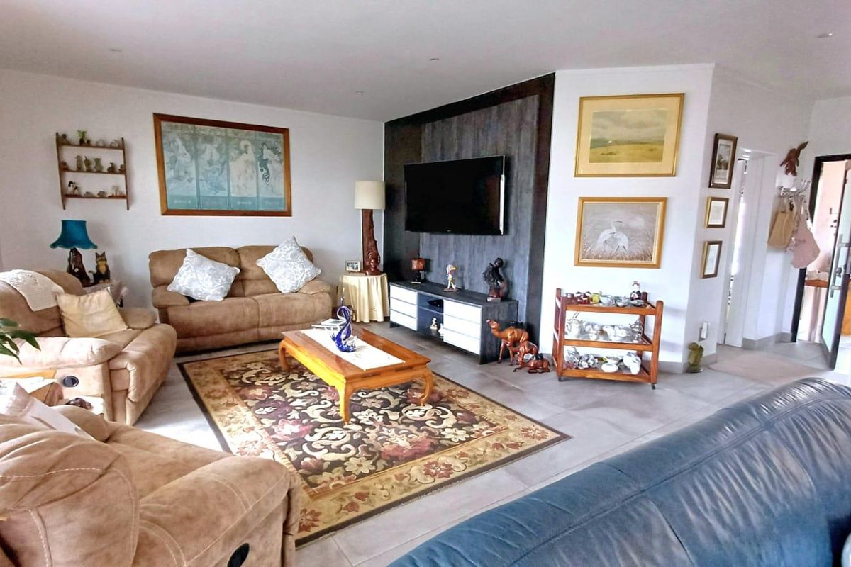 A spacious living room featuring tiled flooring, recessed downlighting, and a modern dark-toned feature wall.