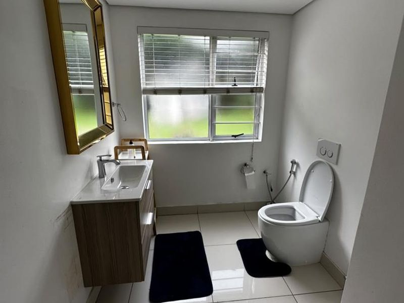 A compact bathroom featuring a wall-mounted vanity with basin, modern toilet with concealed cistern, and tiled flooring.
