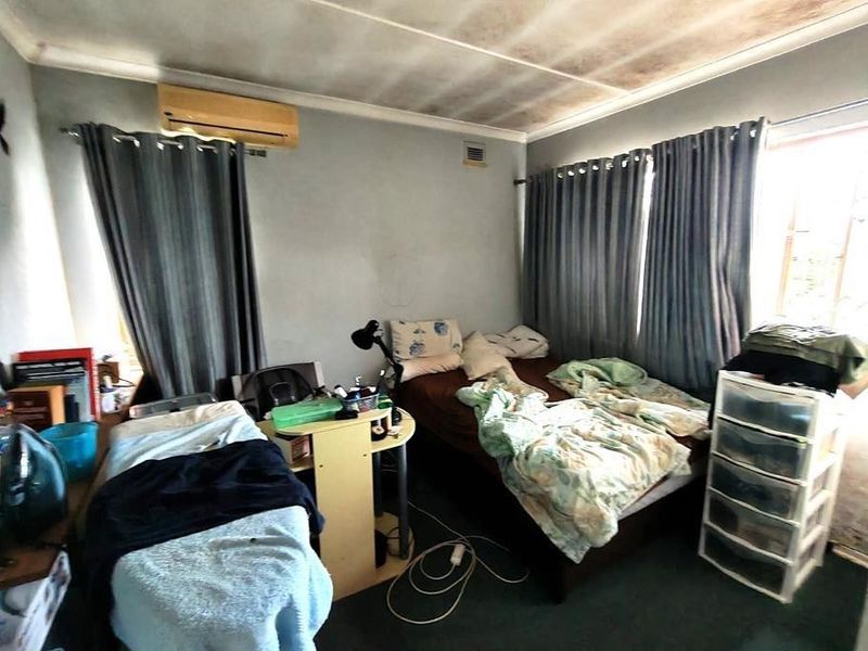 A bedroom featuring a split-system air conditioner and carpet flooring, currently showing significant ceiling water staining and signs of wear requiring maintenance.