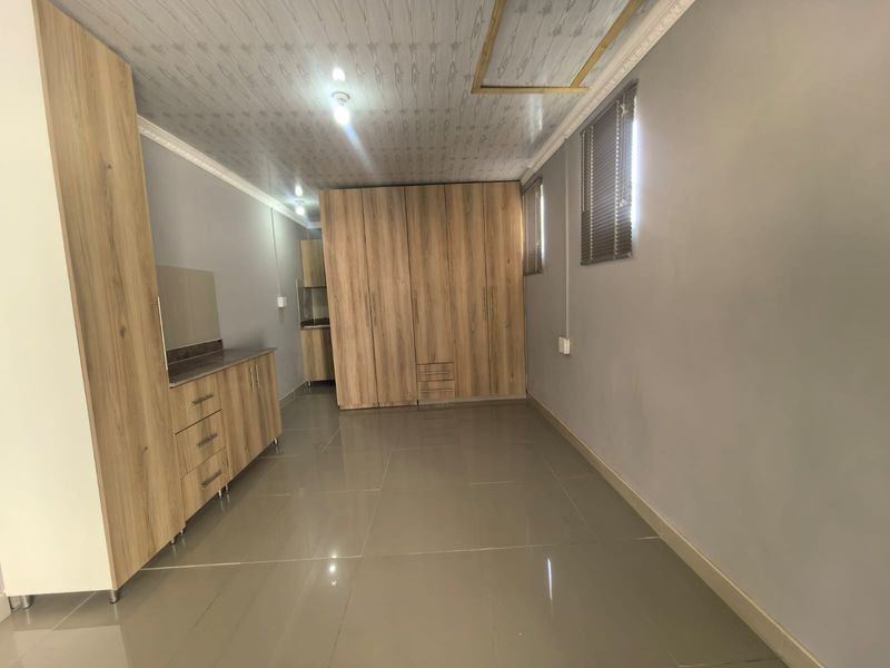 A spacious bedroom featuring extensive built-in wooden cabinetry, large format floor tiles, and neutral grey walls, offering a clean and functional living space.
