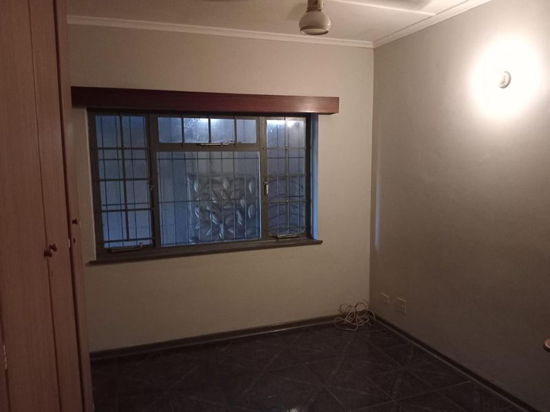 An empty bedroom featuring tiled flooring, a built-in cupboard, and a window fitted with security bars.
