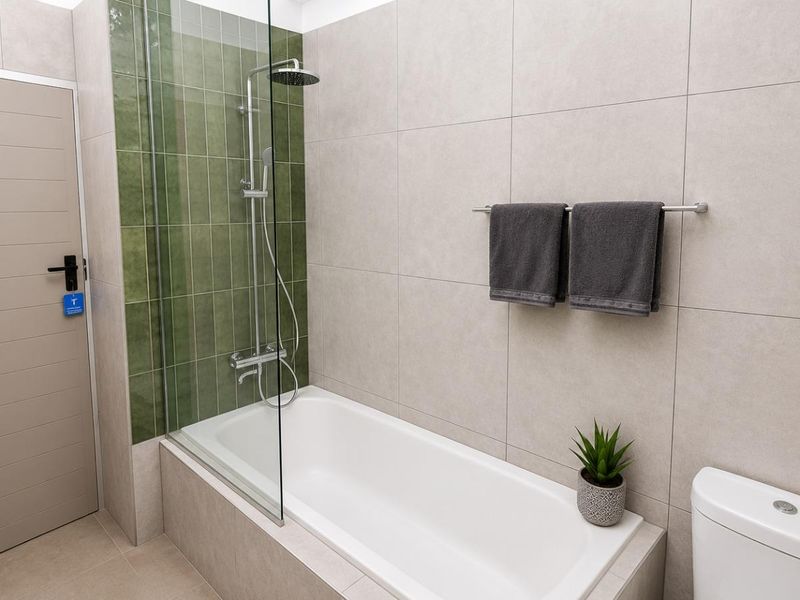 Modern bathroom featuring a built-in bathtub with a glass shower screen, contemporary green accent tiling, and a clean, neutral color palette.