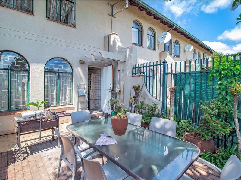 Rear exterior view of the townhouse featuring a paved patio area, arched windows, and perimeter metal security fencing.
