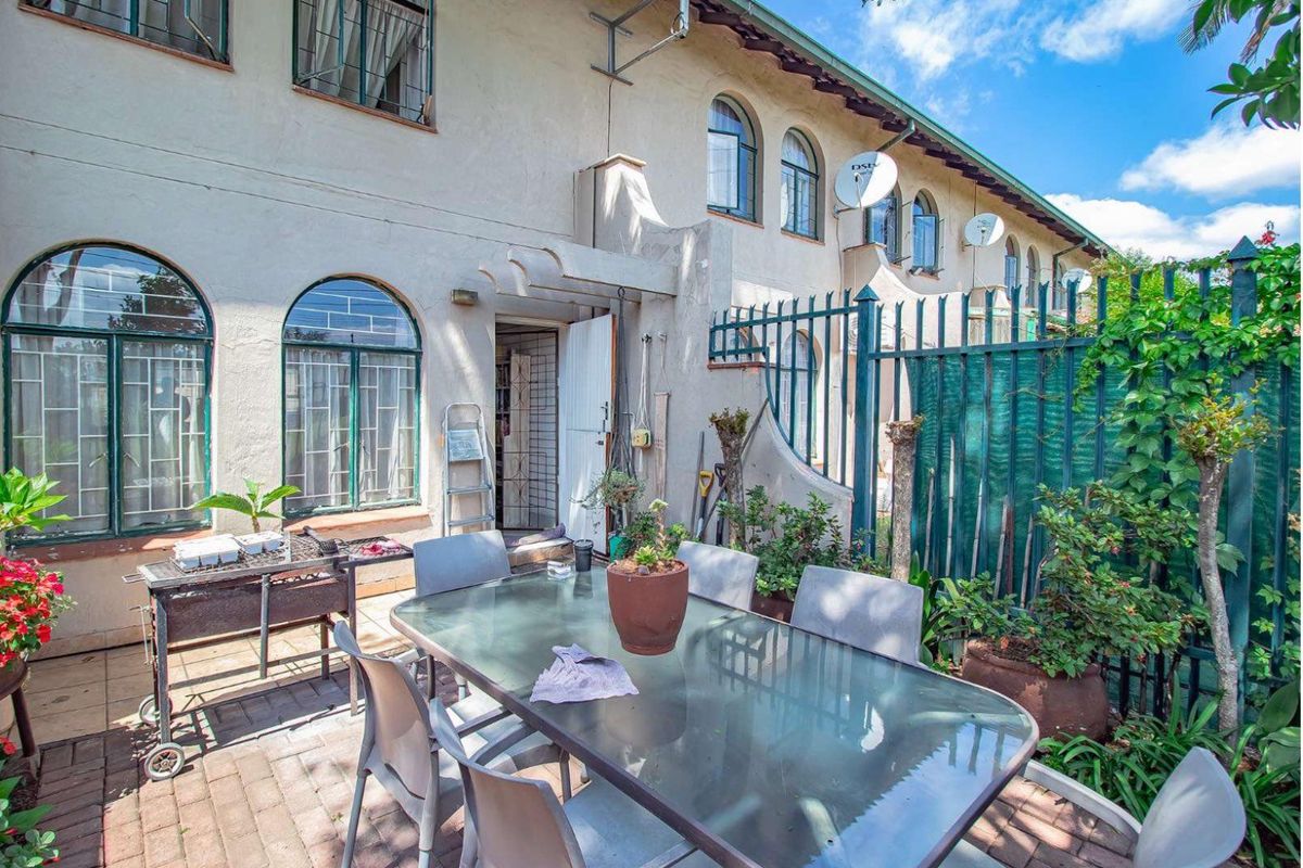 Rear exterior view of the townhouse featuring a paved patio area, arched windows, and perimeter metal security fencing.