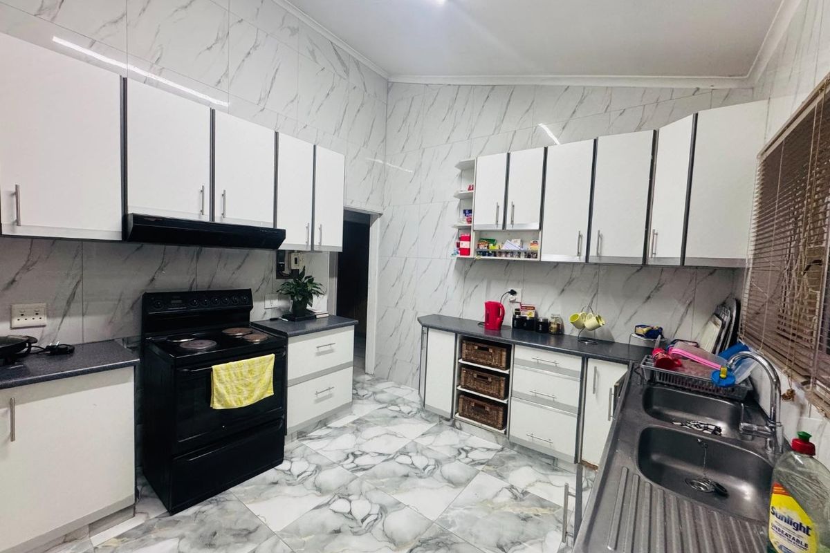 Modern kitchen featuring marble-look wall and floor tiles, ample built-in cabinetry, a double basin sink, and a freestanding stove.