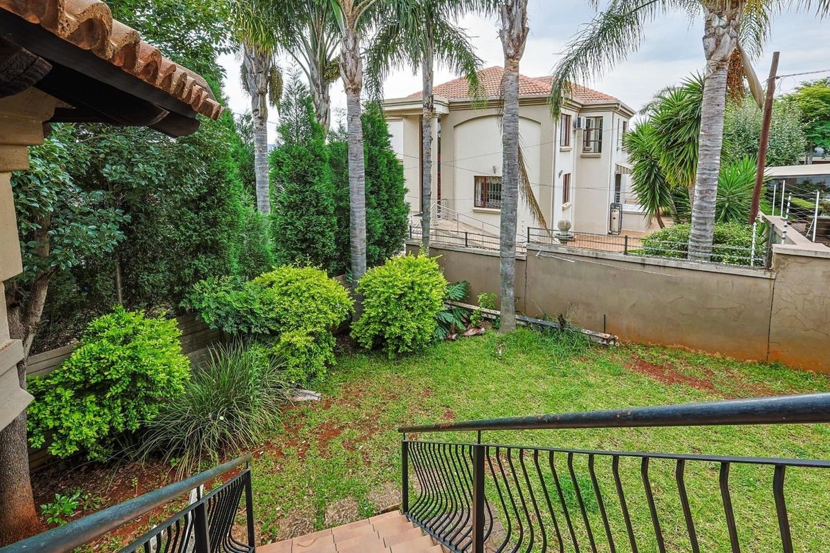 A view of the rear garden area featuring established palm trees, a lawn, and a metal staircase leading down from the patio.