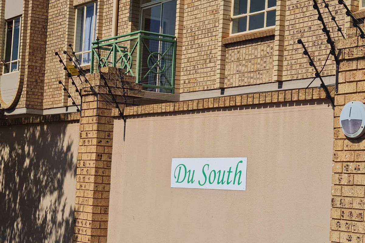 Exterior view of the Du South apartment complex featuring face brick facade, security electric fencing, and a balcony with metal balustrade.