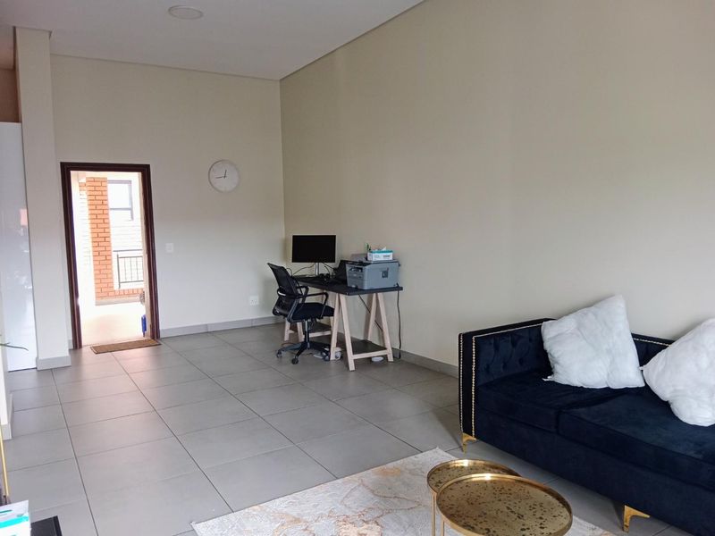 A spacious living area featuring neutral wall tones, large format floor tiles, and recessed ceiling lighting, with direct access to an outdoor balcony.