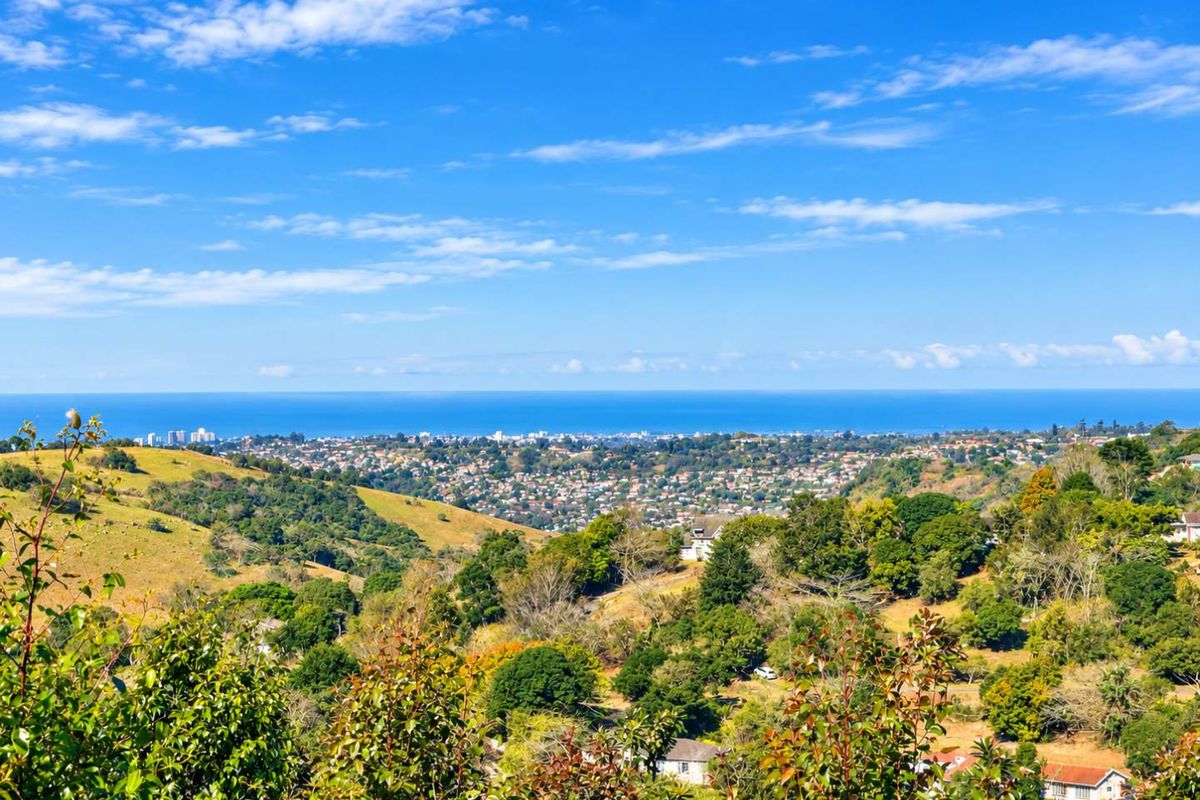 A scenic elevated view overlooking a residential valley with lush greenery and a distant coastal horizon.