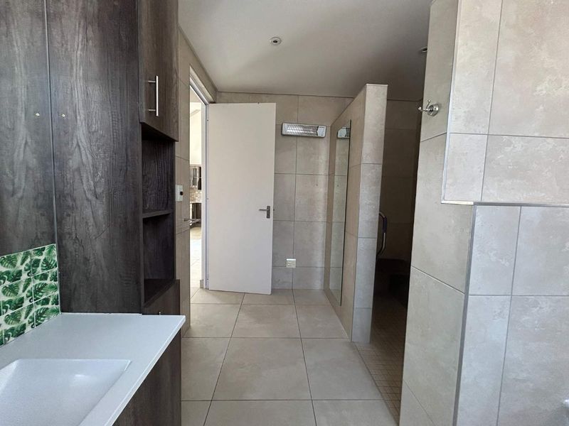 A modern, neutral-toned bathroom featuring a built-in vanity, tiled surfaces, and a walk-in shower area with a wall-mounted heater.