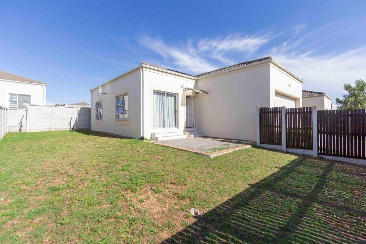 Rear view of the townhouse featuring a private garden, paved patio area, and secure perimeter fencing.