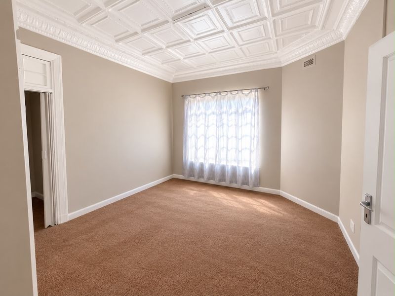 A spacious, empty bedroom featuring a decorative coffered ceiling with crown molding, neutral wall tones, and carpeted flooring.