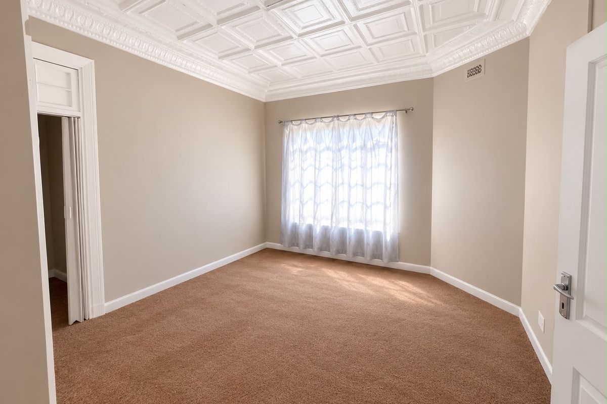 A spacious, empty bedroom featuring a decorative coffered ceiling with crown molding, neutral wall tones, and carpeted flooring.