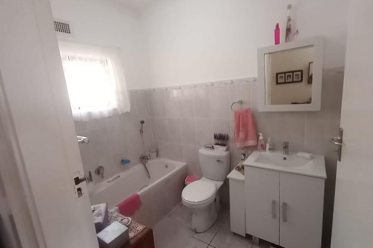 A functional bathroom featuring a bathtub, toilet, and a vanity cabinet with a mirror, finished with neutral wall and floor tiles.