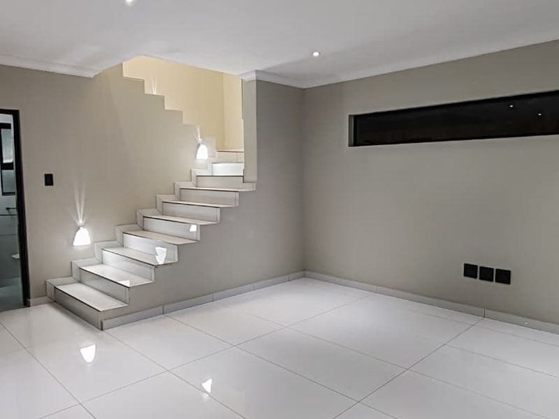 A modern, minimalist living area featuring sleek tiled flooring, a contemporary staircase with integrated lighting, and a horizontal clerestory window.