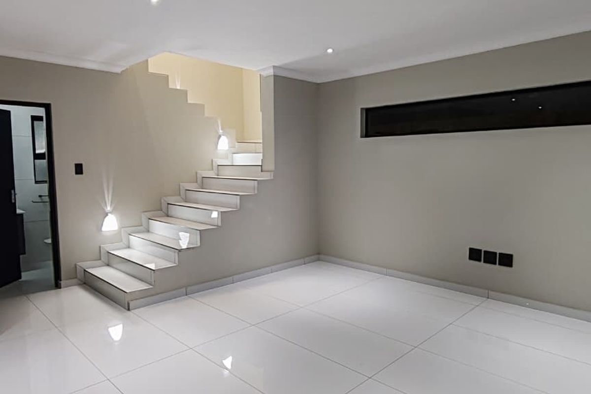 A modern, minimalist living area featuring sleek tiled flooring, a contemporary staircase with integrated lighting, and a horizontal clerestory window.