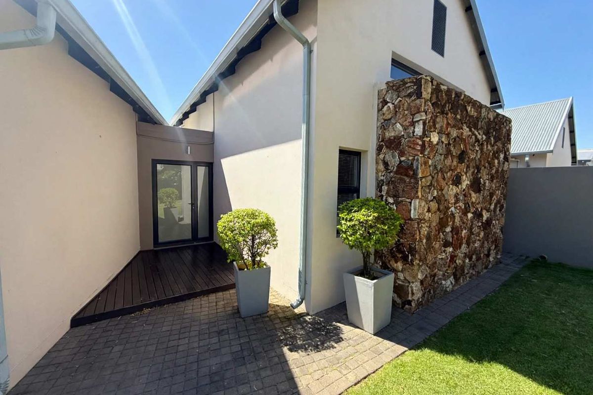 Rear exterior view featuring a stone-clad feature wall, timber decking, and a paved patio area leading to a glass entrance door.