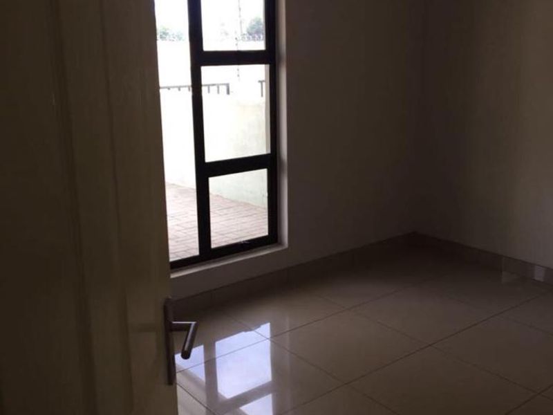 A vacant bedroom featuring neutral tiled flooring and a large aluminium-framed window, providing a clean and blank canvas for interior design.